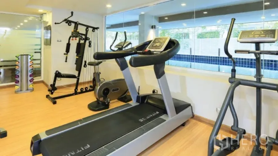 Condominium for rent or sale in Watthana, Bangkok - Condo fitness room with treadmills and weight machines facing the indoor pool.