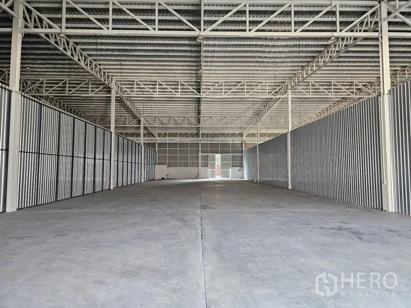 货栈 出租在Khlong Toei, Bangkok - 仓库内部纵深视角，钢梁结构、混凝土地面与后门日光。