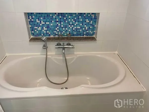 Condominium for sale in Phra Khanong, Bangkok - Bathroom with built-in bathtub, handheld shower, and blue mosaic accent niche.