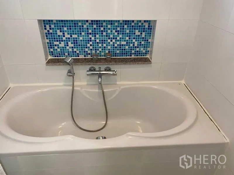 Condominium for sale in Phra Khanong, Bangkok - Bathroom with built-in bathtub, handheld shower, and blue mosaic accent niche.