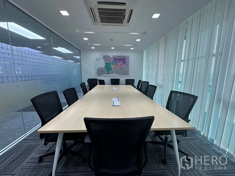 Office Space for rent - Glass-walled meeting room with a long table, mesh chairs and vertical blinds under cassette AC.