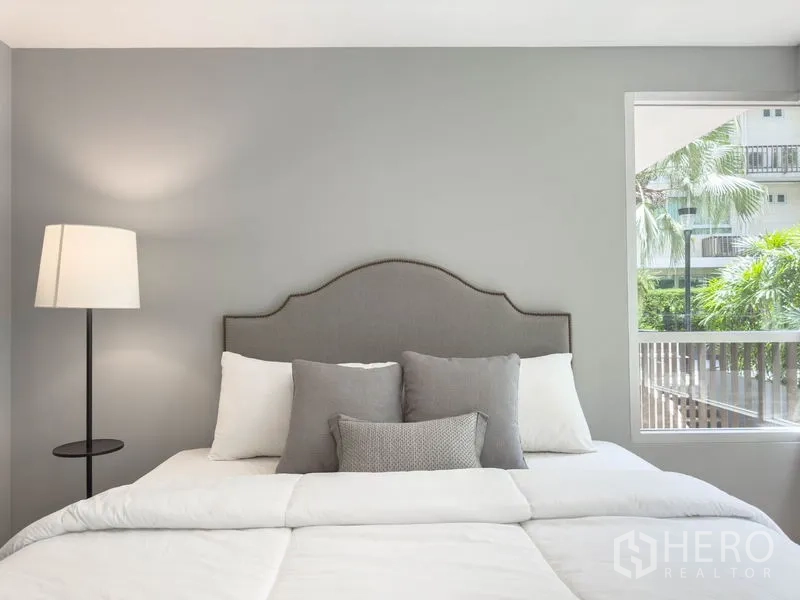 Condominium for sale in Watthana, Bangkok - Cozy bedroom with upholstered headboard, floor lamp, and window.