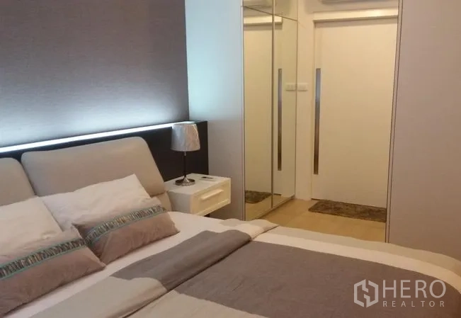 Condominium for rent or sale in Watthana, Bangkok - Cozy bedroom angle showing bed, mirrored wardrobe, sliding closet doors and soft ambient lighting.