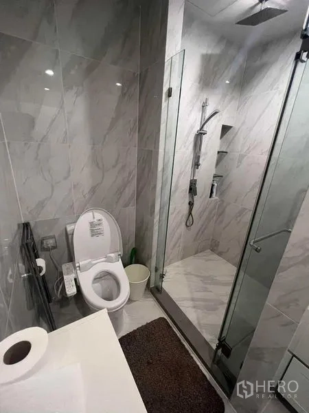 公寓 出售在Ratchathewi, Bangkok - 大理石纹浴室，玻璃淋浴间与顶喷花洒，旁为坐便器。