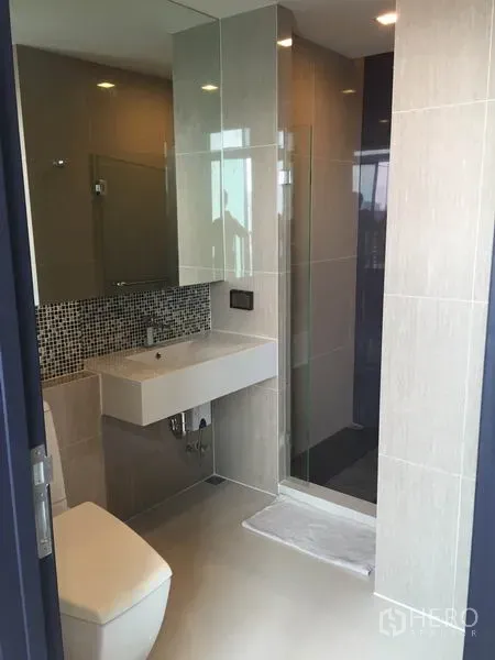 คอนโด ให้เช่าในKhlong Toei, Bangkok - ห้องน้ำสมัยใหม่พร้อมตู้กระจกกั้นอาบน้ำ อ่างล้างหน้าแขวนผนัง และกระเบื้องโทนอบอุ่น