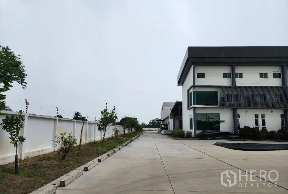 Factory for rent or sale in Sai Noi, Nonthaburi - Modern factory exterior with a two-storey office block, wide concrete driveway, and walled compound with landscaping.