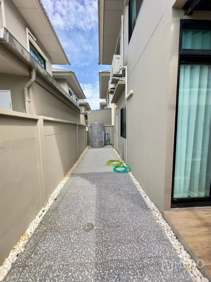 独立式住宅 出租在Samut Prakan - 房屋侧边实用通道，铺地砖，设蓄水罐与花园水管。