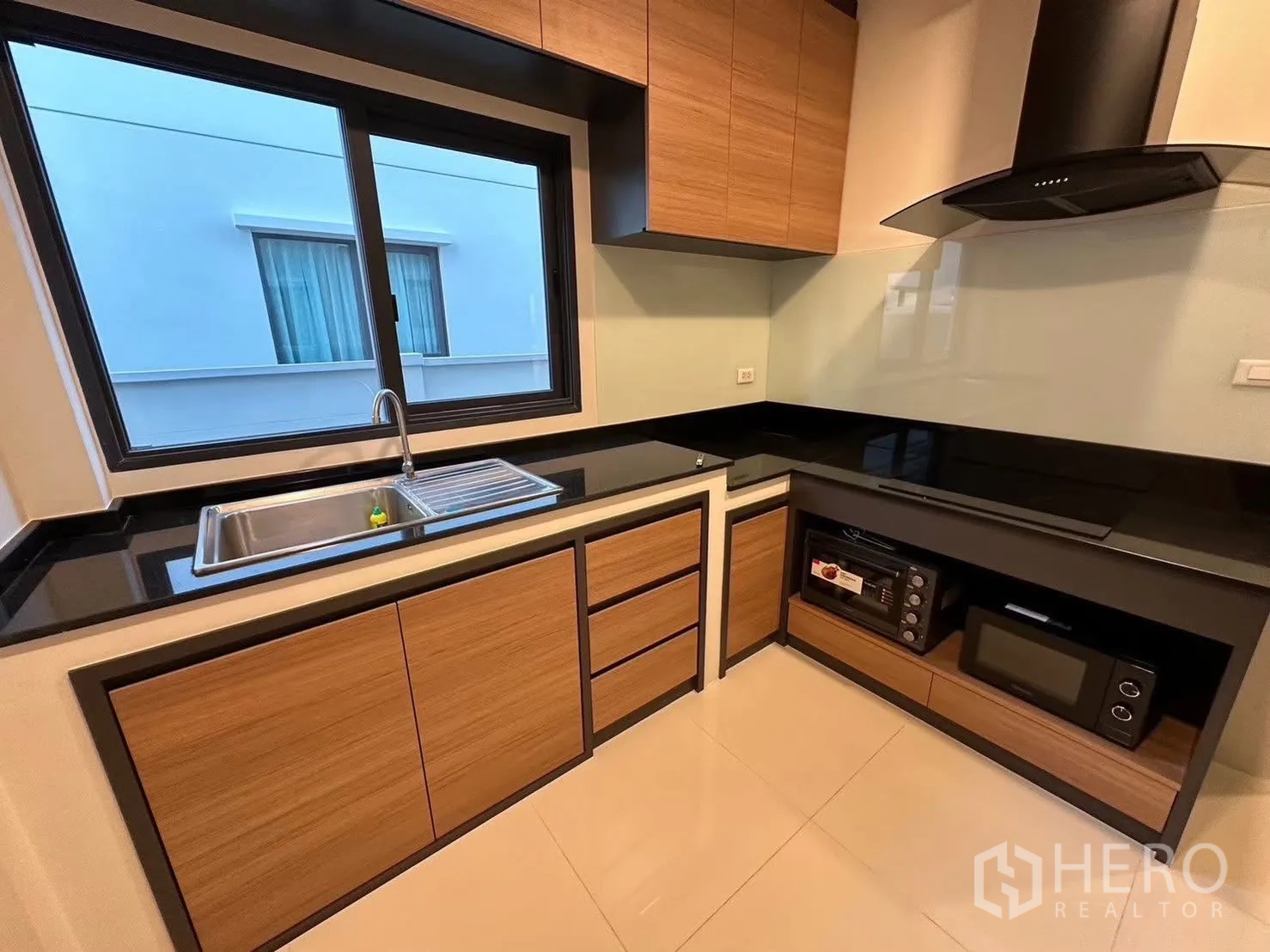 Detached House for rent in Bang Phli, Samut Prakan - Modern L-shaped kitchen with black countertops, wood cabinetry and a window.