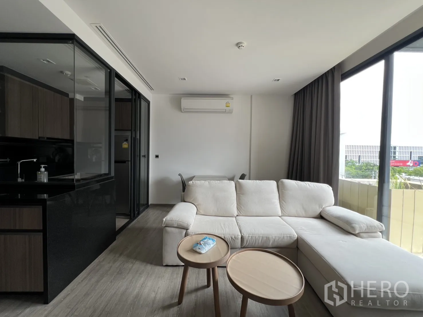 公寓 for rent in Watthana, Bangkok - 明亮客厅配米色转角沙发、套几与大窗帘窗户。