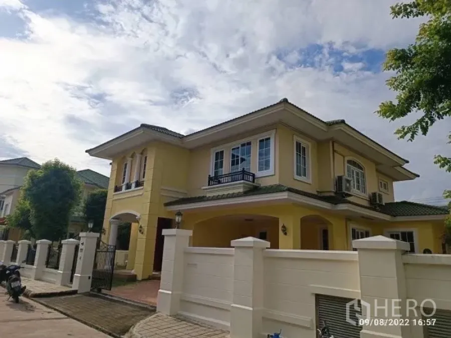 独立式住宅 出售在Prawet, Bangkok - 黄色独栋别墅前景，再现大门与车道。