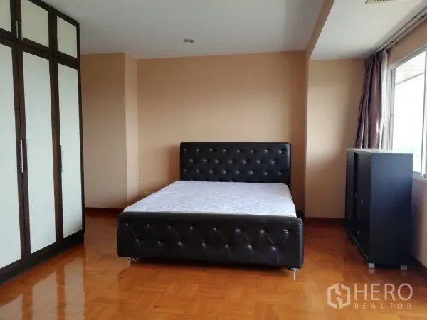 Condominium for rent in Watthana, Bangkok - Spacious bedroom with black tufted bed, large built‑in wardrobes and glossy wooden floors in a Watthana Bangkok condo.