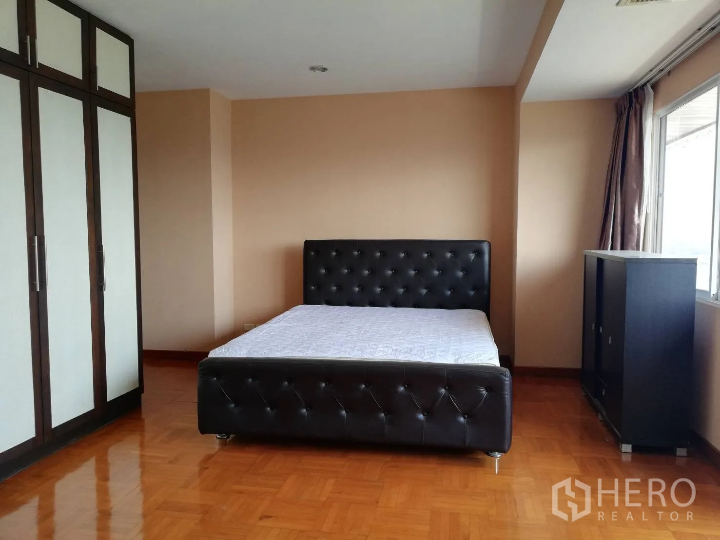 Condominium for rent in Watthana, Bangkok - Spacious bedroom with black tufted bed, large built‑in wardrobes and glossy wooden floors in a Watthana Bangkok condo.