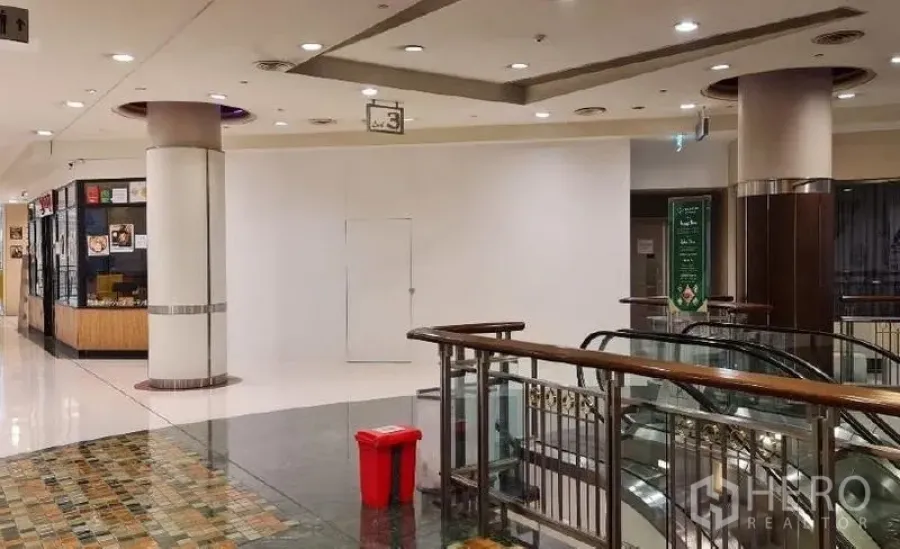 พื้นที่ขายปลีก ให้เช่า - โถงศูนย์การค้าพร้อมหน้าร้านว่างผนังสีขาวข้างราวบันไดเลื่อนและพื้นเงา