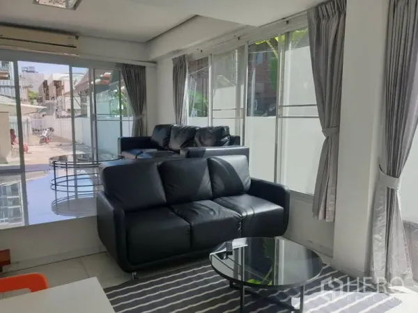 Detached House for rent in Khlong Toei, Bangkok - Sunlit lounge with two black sofas, striped rug and wraparound windows.