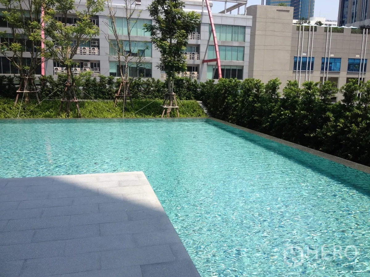 Condominium for rent in Watthana, Bangkok - Outdoor swimming pool surrounded by greenery within the condominium.