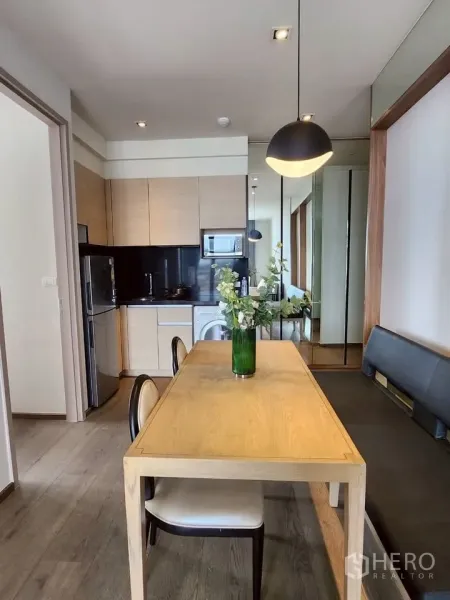 Condominium for rent in Khlong Toei, Bangkok - Modern open kitchen with light wood cabinets, black backsplash, dining table and pendant light, plus fridge, microwave and washer.