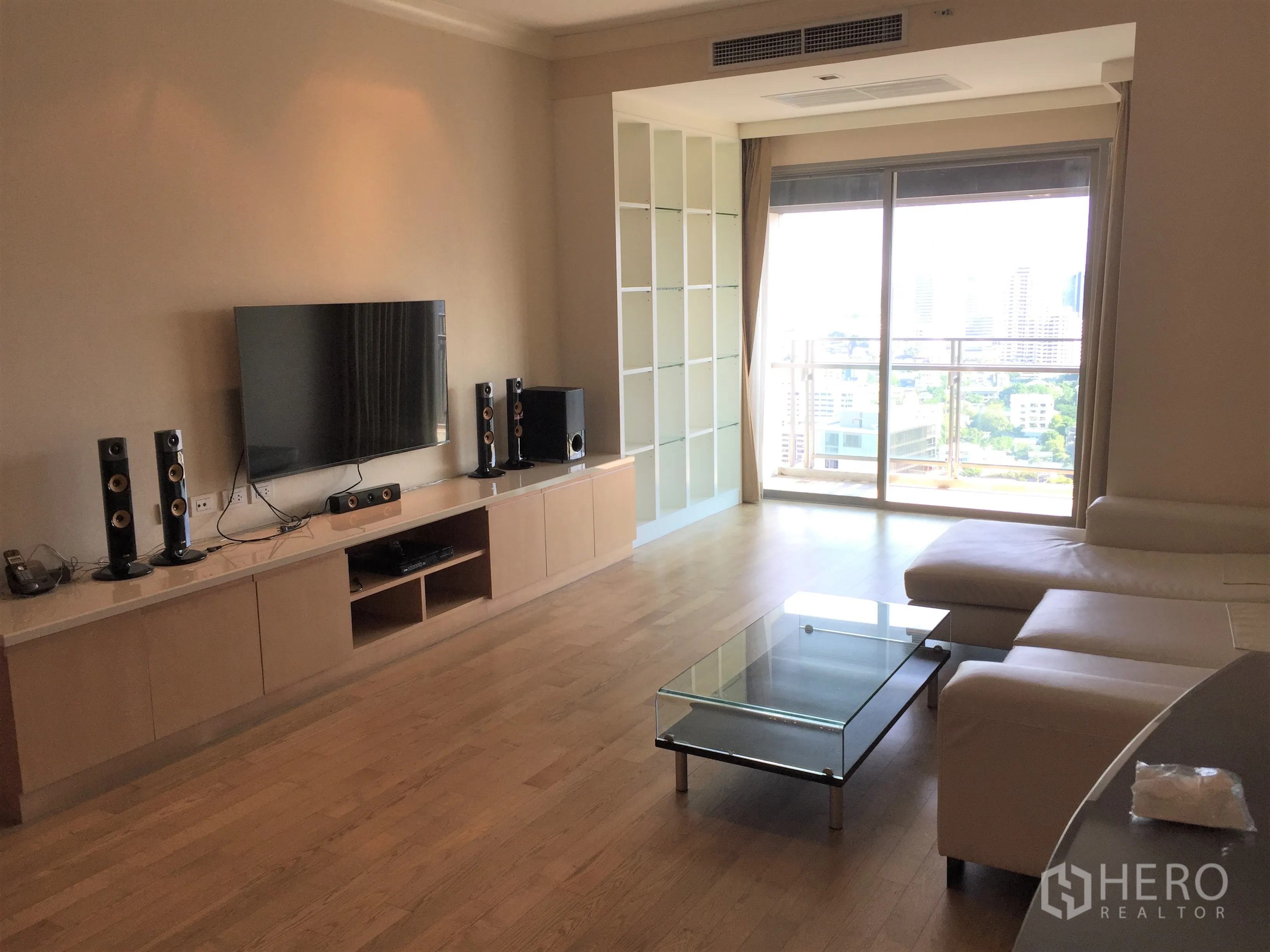 คอนโด ให้เช่าในWatthana, Bangkok - ห้องนั่งเล่นกว้างติดทีวีบนผนัง ตู้วางสื่อ โต๊ะกลางกระจก และระเบียงวิวเมือง