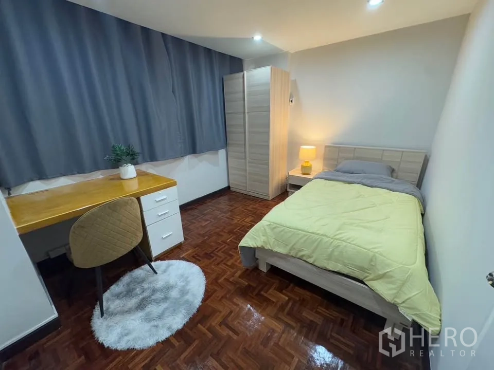 Condominium for rent in Huai Khwang, Bangkok - Secondary bedroom featuring a single bed, study desk, wardrobe and bedside lamp with grey curtains.