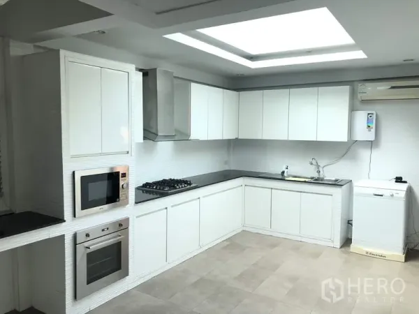 Detached House for rent in Suan Luang, Bangkok - Modern L-shaped white kitchen with built-in oven, gas hob, hood and skylight