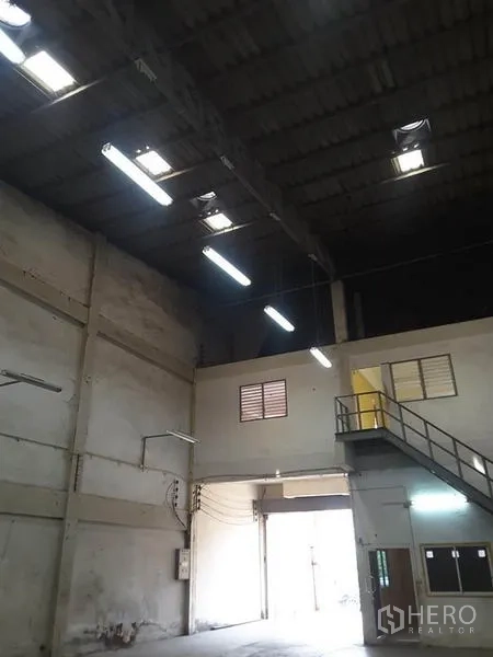 Factory for rent in Mueang Ratchaburi, Ratchaburi - High-roof factory bay showing hanging lights, ventilation windows and stair access to office.