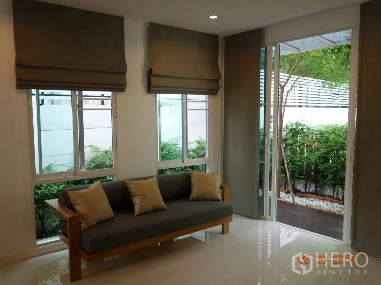 Townhouse for rent or sale in Suan Luang, Bangkok - Living room with sofa, multiple windows and doors opening to a patio.