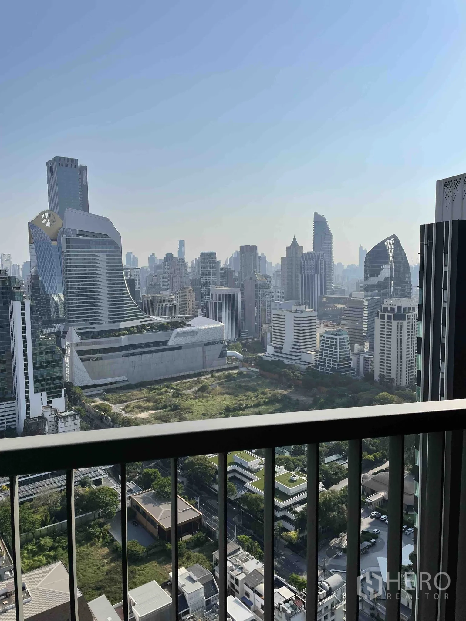 Condominium for rent in Pathum Wan, Bangkok - Balcony railing framing a panoramic Bangkok skyline and open green plots below.