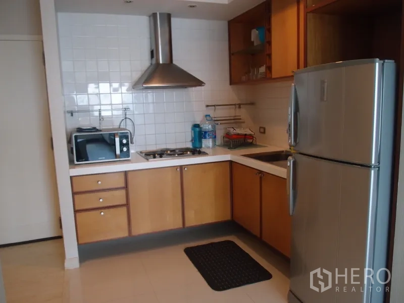 Condominium for rent in Sathon, Bangkok - Modern L-shaped kitchen with stainless refrigerator, gas hob, range hood, microwave, and white tile backsplash in a Sathon condominium.