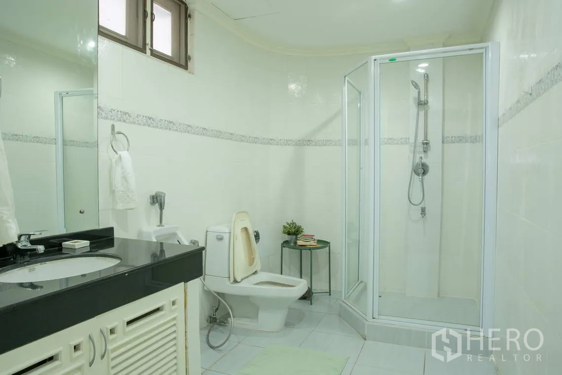 Apartment for rent in Khlong Toei, Bangkok - Bathroom with glass shower enclosure, toilet, and wide vanity.