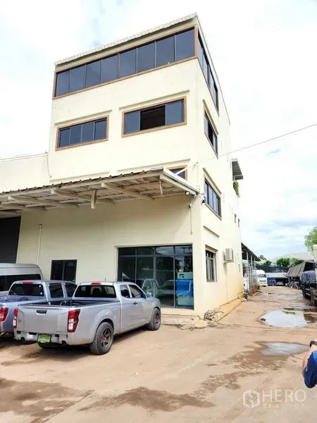 Warehouse for rent in Bang Kruai, Nonthaburi - Four-storey office block attached to the warehouse with pickup trucks parked in front.
