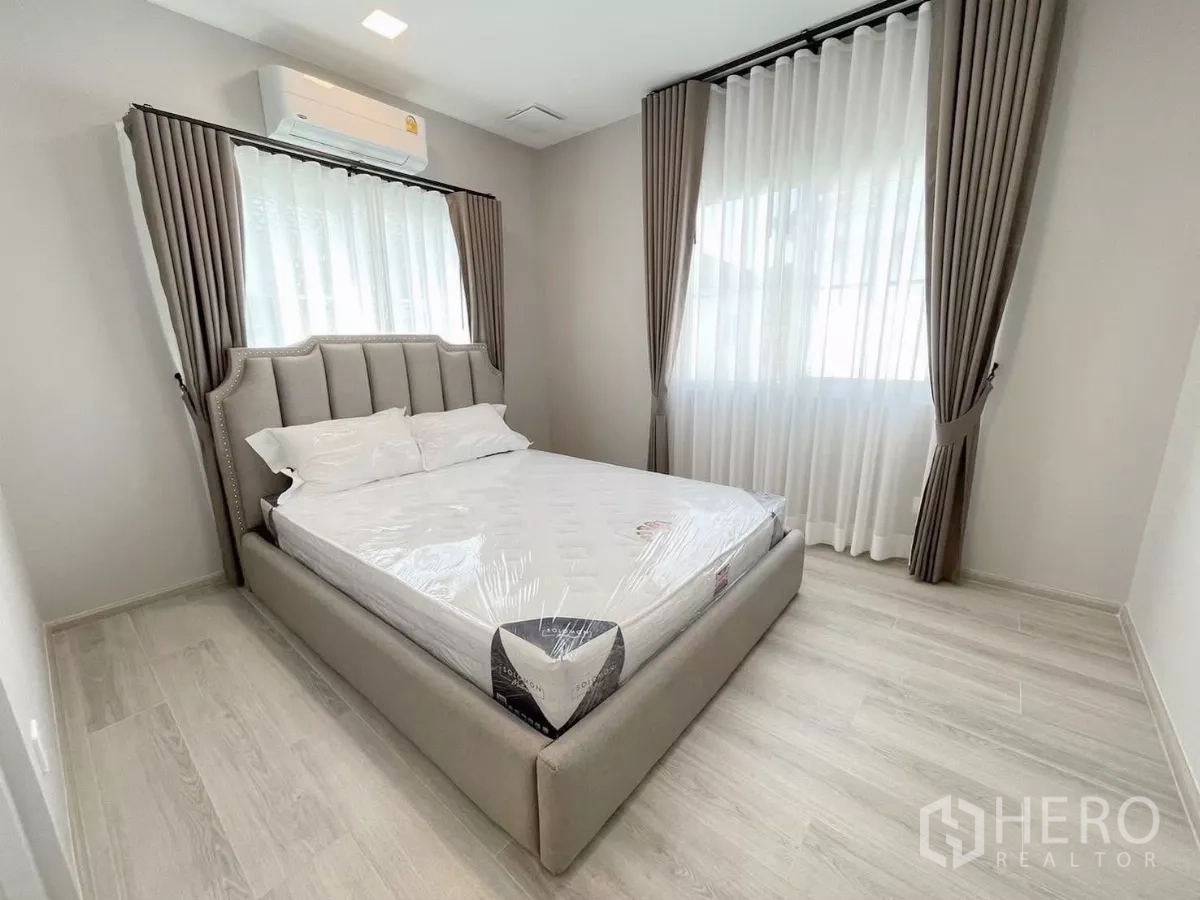 Detached House for rent in Bang Phli, Samut Prakan - Cozy bedroom with upholstered bedframe, air conditioner, and two windows.