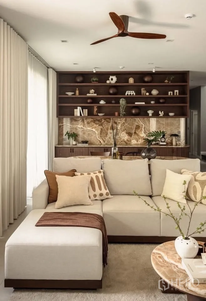 Detached House for rent or sale in Lat Krabang, Bangkok - Beige sectional sofa with patterned cushions facing shelving and a stone backsplash.