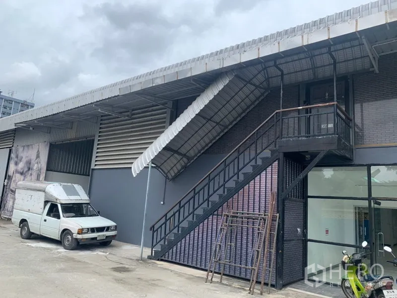 货栈 出租在Suan Luang, Bangkok - 仓库外立面，金属楼梯、雨棚与停车区
