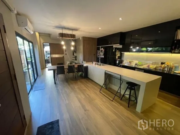 ทาวน์เฮาส์ ขายในBang Phli, Samut Prakan - ครัวสไตล์โอเพ่นพร้อมไอส์แลนด์ยาว ตู้สีดำ ไฟแขวน และพื้นลายไม้ติดประตูกระจกบานเลื่อน.