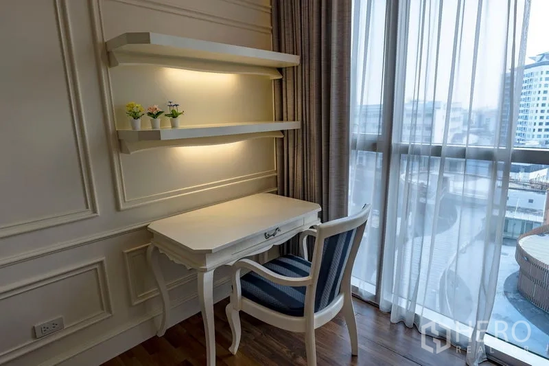 Condominium for rent in Watthana, Bangkok - Workstation with lit floating shelves and striped chair next to sheer curtains and city-view windows.