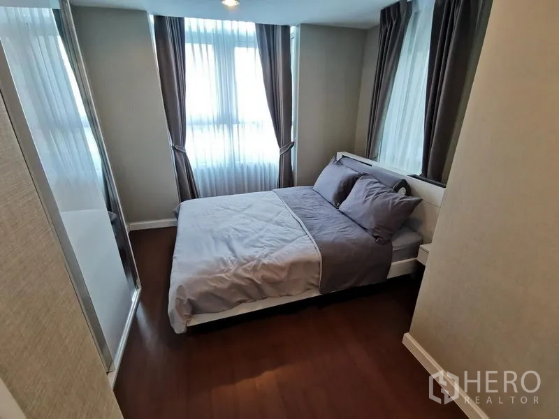 Condominium for rent or sale in Huai Khwang, Bangkok - Cozy bedroom with double bed, corner windows and sheer curtains.