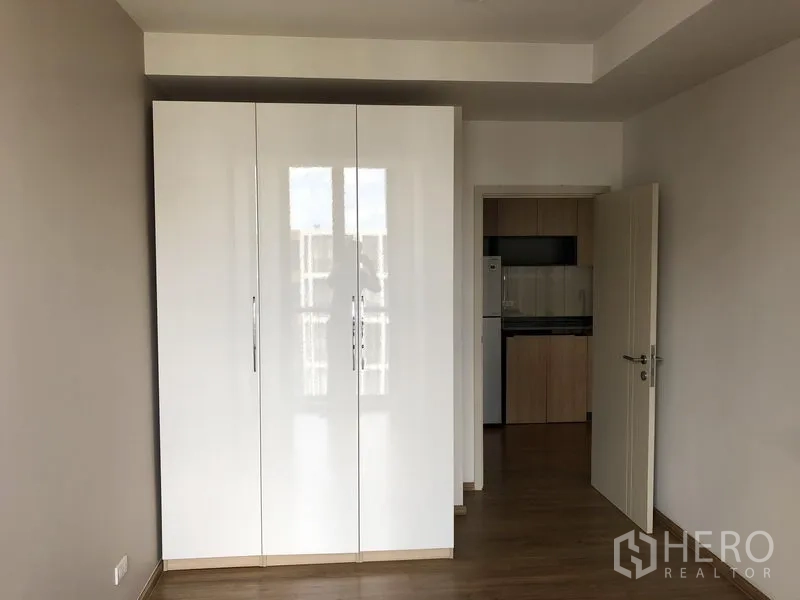 Condominium for rent in Watthana, Bangkok - Second bedroom with glossy white wardrobe and doorway leading to the kitchen area.