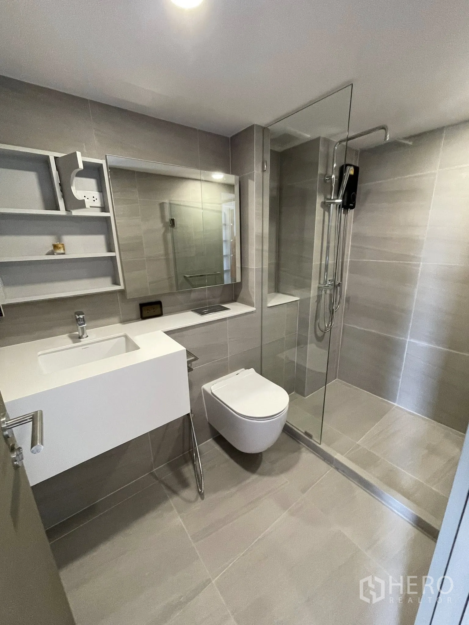 Condominium for rent in Khlong Toei, Bangkok - Modern bathroom with floating vanity, wall-mounted toilet, and glass-enclosed shower.
