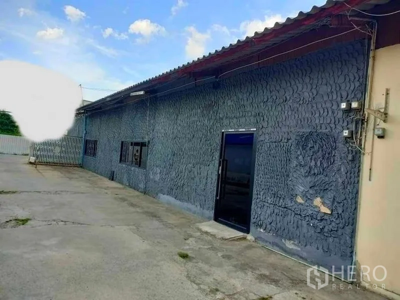 Warehouse for rent in Suan Luang, Bangkok - Warehouse exterior with corrugated roof, rough-finish walls and wide driveway for loading and parking.