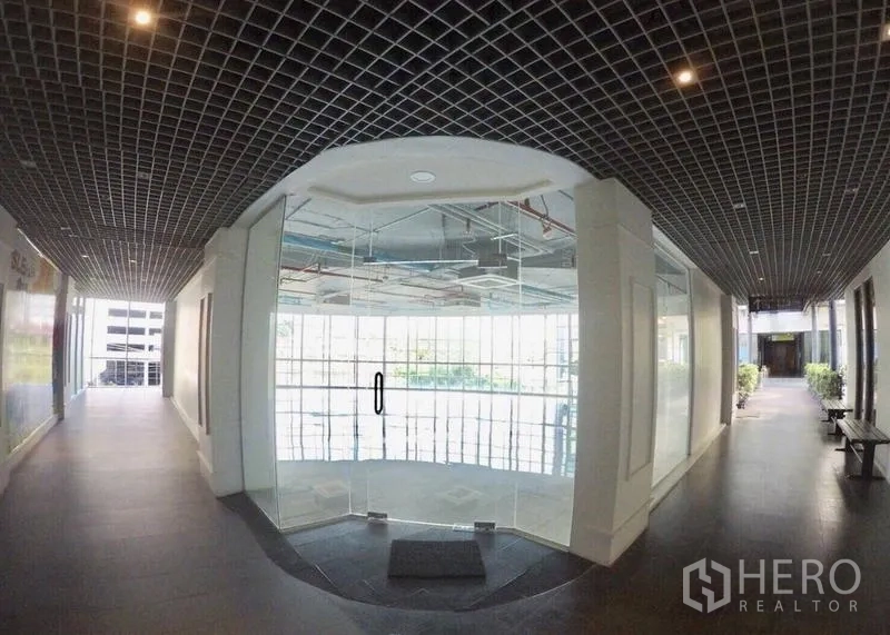 零售空间 出租在Khlong Toei, Bangkok - 大楼走廊与玻璃门店入口，现代格栅天花设计。