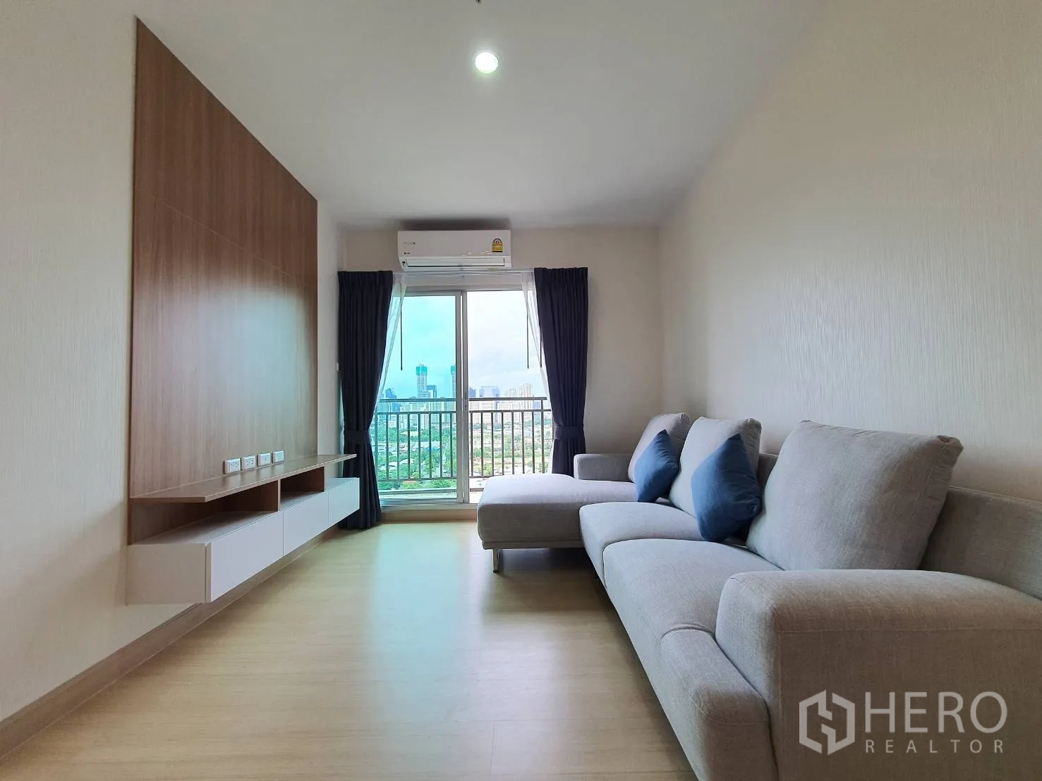 คอนโด for rent in Huai Khwang, Bangkok - มุมมองยาวจากห้องนั่งเล่นสู่ระเบียง โซฟาแอลด้านขวาและผนังไม้ด้านซ้าย