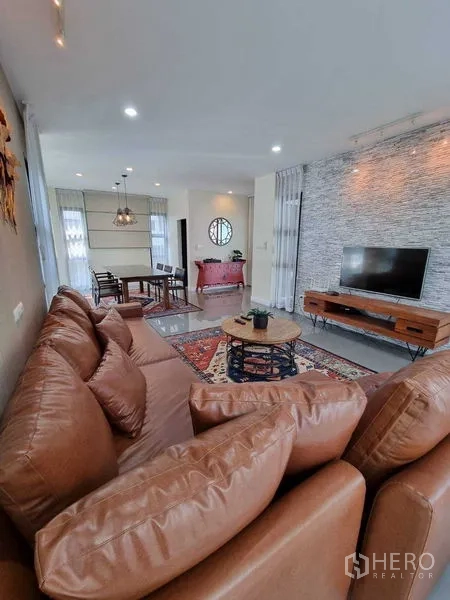 独立式住宅 出租或出售在Prawet, Bangkok - 开放式客餐厅，皮沙发、电视和装饰墙面。