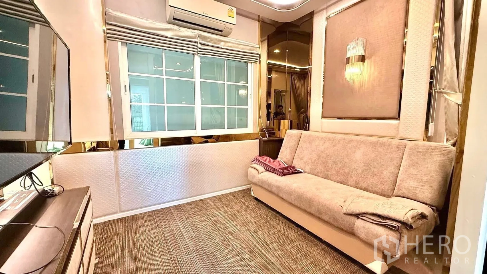 Detached House for rent or sale in Bueng Kum, Bangkok - Family lounge with beige sofa, wall-mounted TV, air conditioner and carpeted floor.