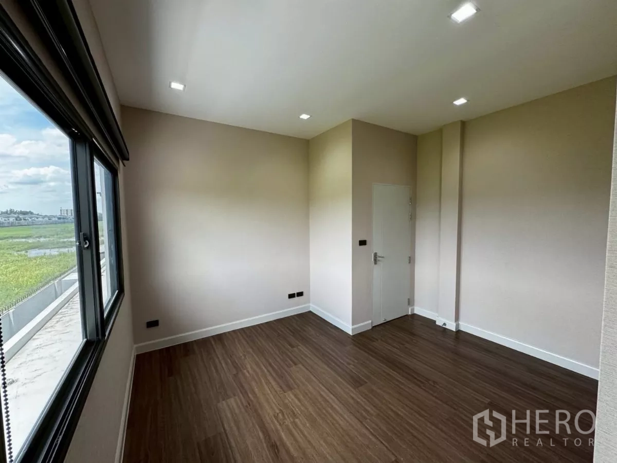 บ้าน ให้เช่าหรือขายในLat Krabang, Bangkok - ห้องอเนกประสงค์สว่าง มีหน้าต่างบานกว้าง พื้นไม้ มองเห็นพื้นที่สีเขียว.