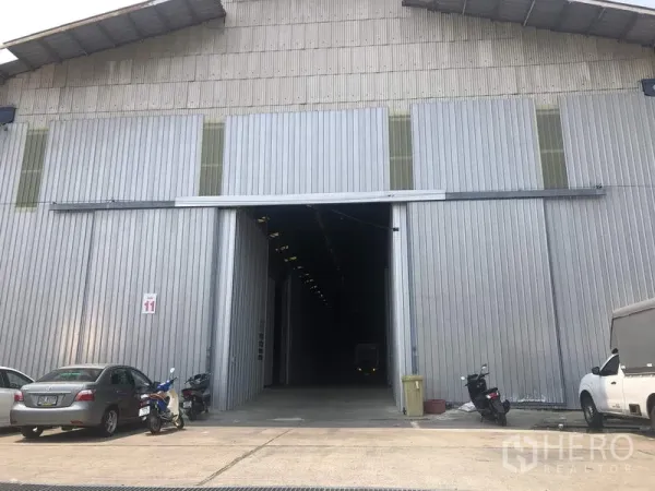 คลังสินค้า ให้เช่าในPak Kret, Nonthaburi - ประตูบานเลื่อนขนาดใหญ่ของโกดังผนังเมทัลชีท พร้อมลานจอดรถด้านหน้า ในปากเกร็ด นนทบุรี