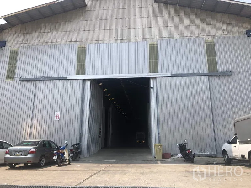 คลังสินค้า ให้เช่าในPak Kret, Nonthaburi - ประตูบานเลื่อนขนาดใหญ่ของโกดังผนังเมทัลชีท พร้อมลานจอดรถด้านหน้า ในปากเกร็ด นนทบุรี