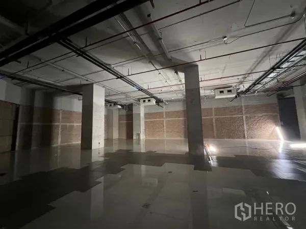 พื้นที่ขายปลีก ให้เช่า - มุมมองกว้างของพื้นที่ร้านค้ายังไม่ตกแต่ง มีเสาหลายต้นและท่อระบบเหนือศีรษะ