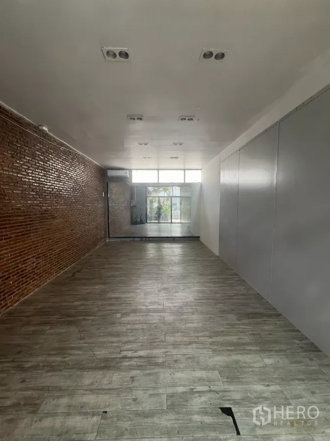 พื้นที่ขายปลีก ให้เช่า - โถงขายของทรงยาว ผนังอิฐเปลือย ผนังสีเทา และพื้นลายไม้