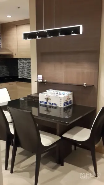 Condominium for rent in Mueang Samut Prakan, Samut Prakan - Dining corner with a four-seat table and linear pendant light adjoining a modern kitchen with mosaic backsplash.