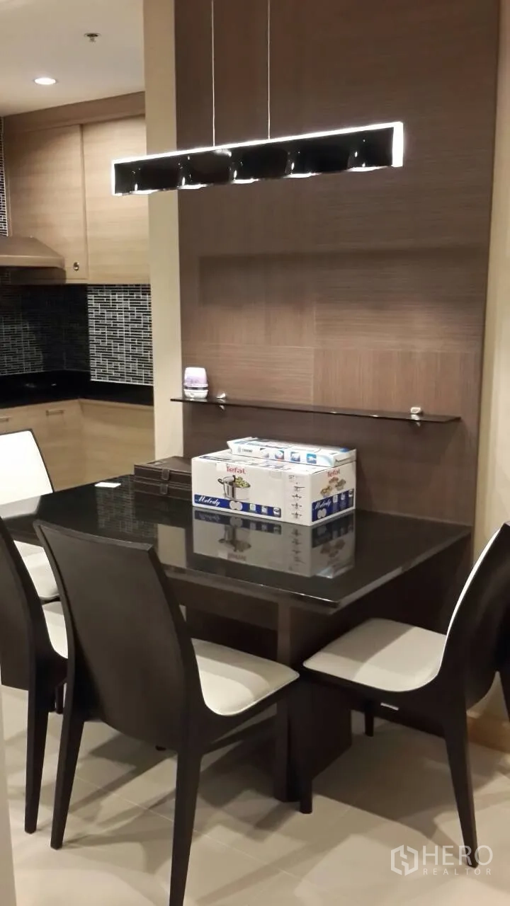 Condominium for rent in Mueang Samut Prakan, Samut Prakan - Dining corner with a four-seat table and linear pendant light adjoining a modern kitchen with mosaic backsplash.