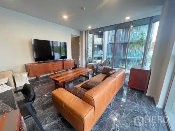 Condominium for rent in Watthana, Bangkok - Another angle of the bright living room with leather sofa, big TV and wall-to-wall windows.